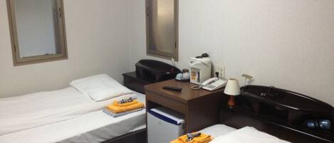 A hotel room with two single beds, a desk with a telephone and a lamp, a coffee maker, and a mirror on the wall.