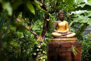 A statue of a seated figure in a meditative pose, surrounded by lush greenery.