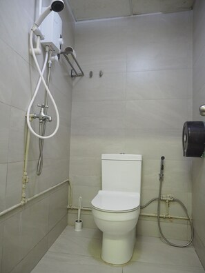 A small, tiled bathroom with a toilet, a shower unit, and a toilet paper holder. - Pillow Talk Hostel (Singapore)