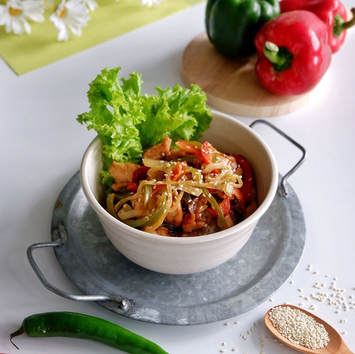 Un bol de légumes et de viande sautés, parsemés de graines de sésame, servis sur une assiette blanche avec de la laitue.
