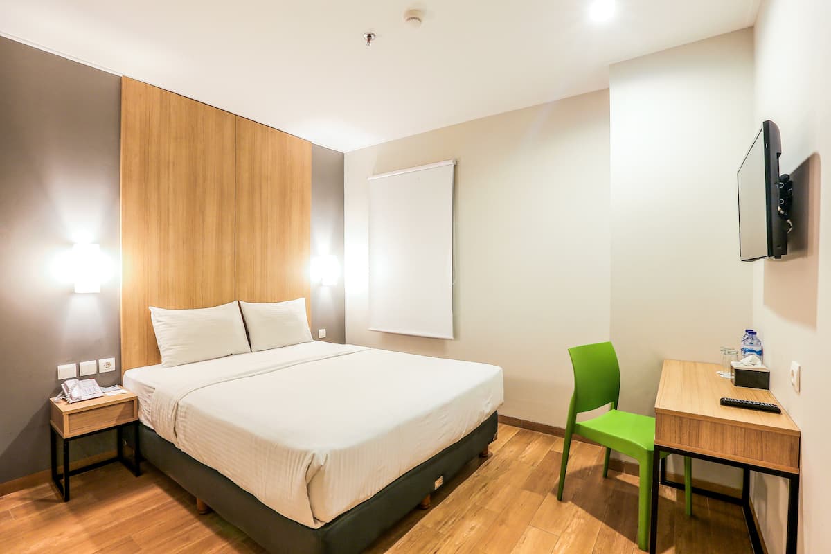 A hotel room with a bed, a desk, a chair, a TV mounted on the wall, and a wooden panel on the wall.