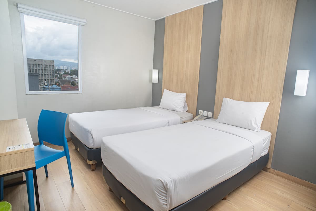 A hotel room with two beds, a desk, a chair, and a window with a city view.