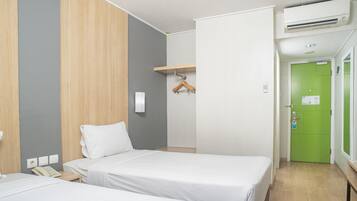 A hotel room with two beds, a wooden panel wall, a green door, and a small table with a telephone.