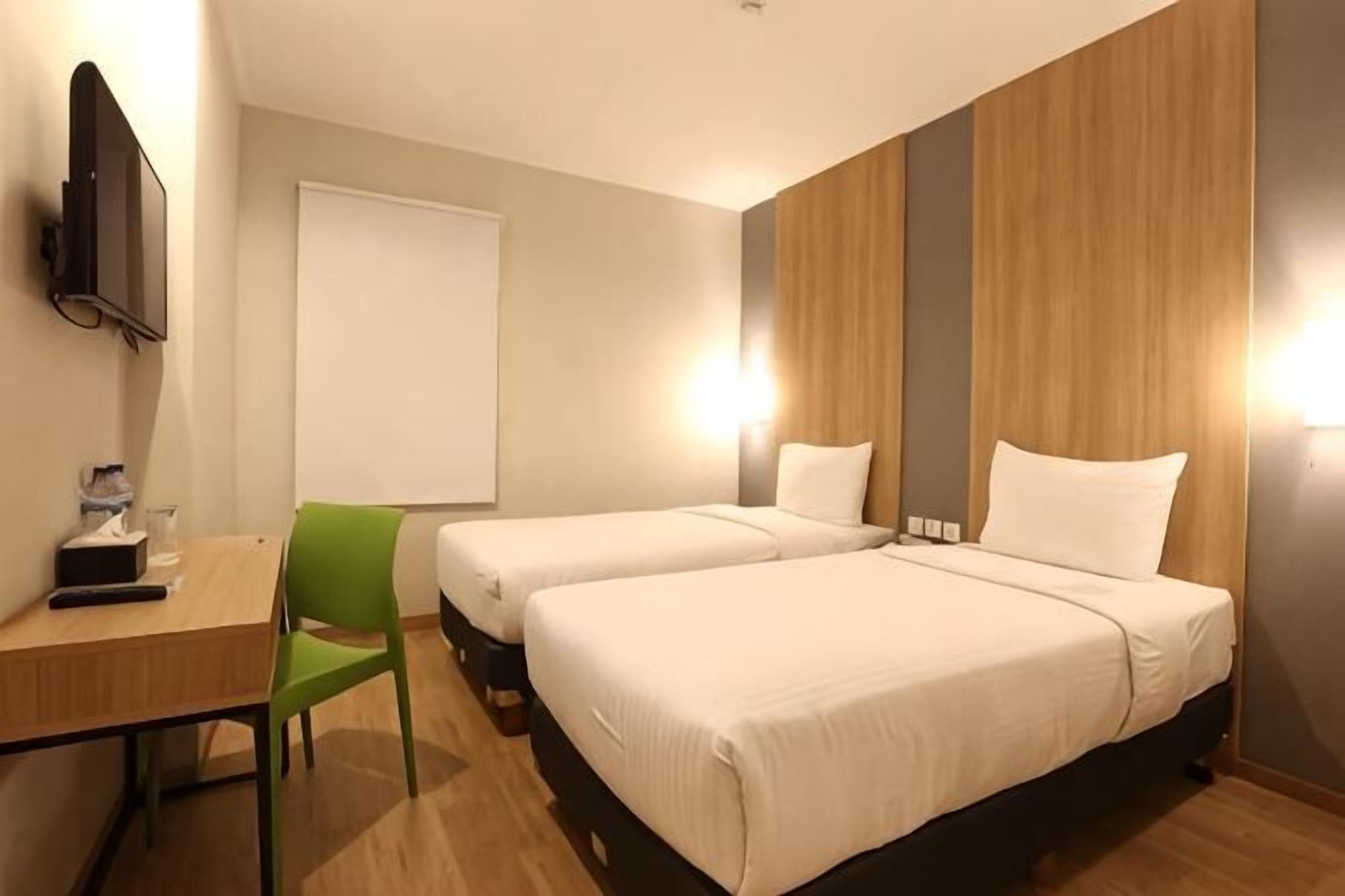 A hotel room with two beds, a desk, a chair, a TV, and a window.