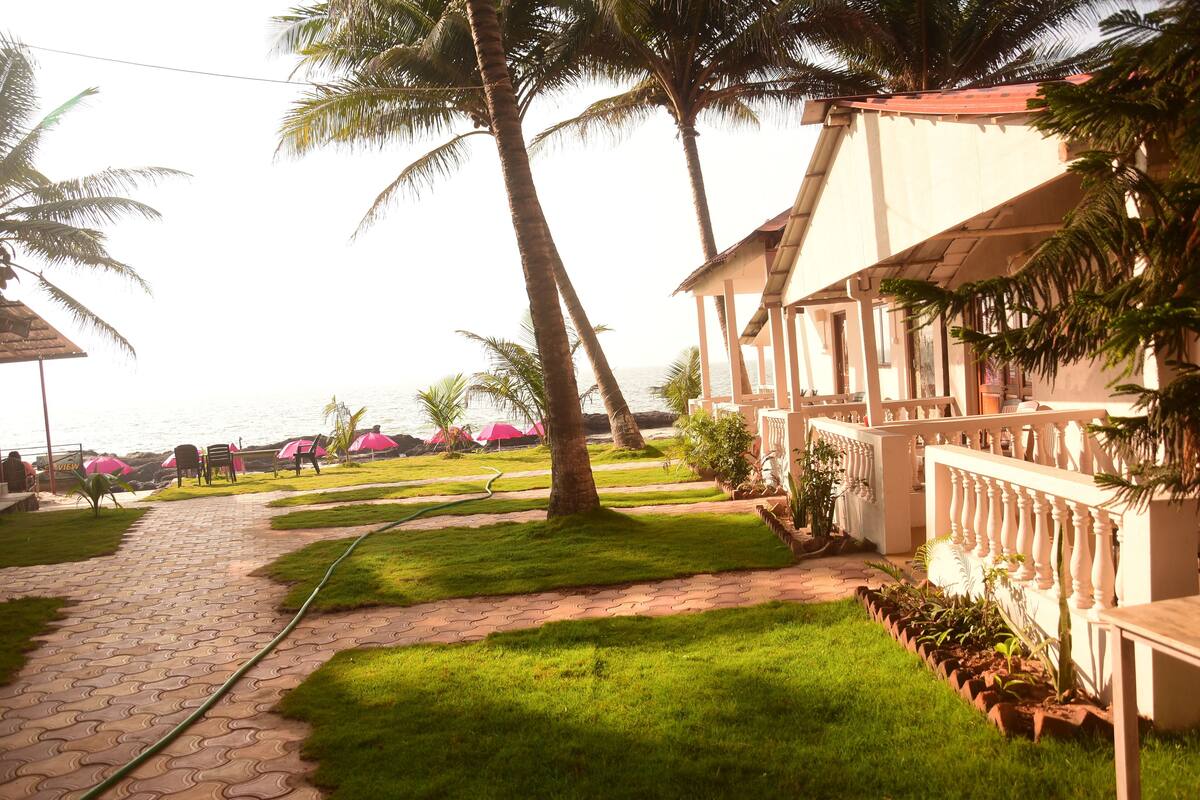 A pathway leading to a beach area with palm trees, a covered seating area, and a building with a balcony.