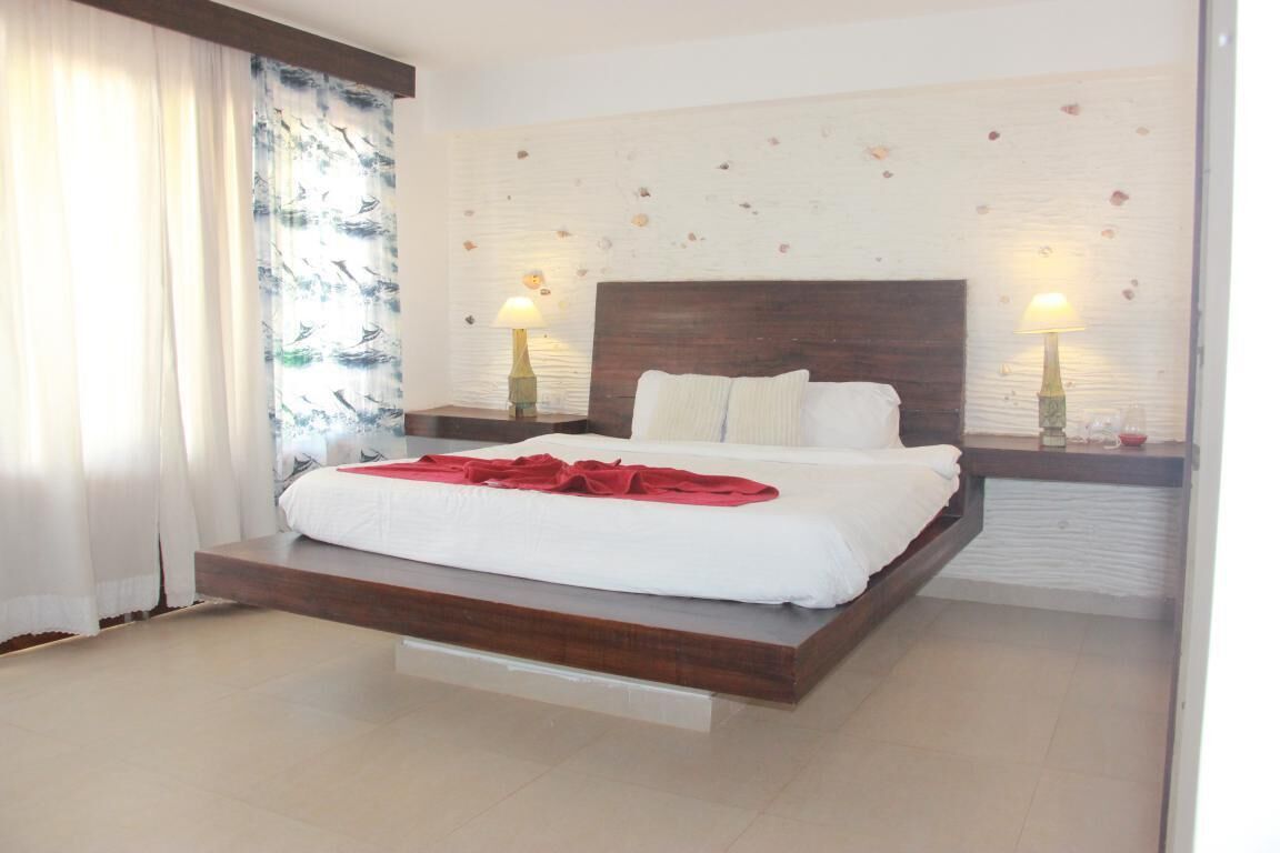 A modern bedroom with a wooden platform bed, white linens, two bedside lamps, and a decorative wall with small items.