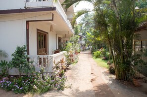 A narrow pathway flanked by potted plants and a white building with a balcony. - Sea View Resort (Ashvem)