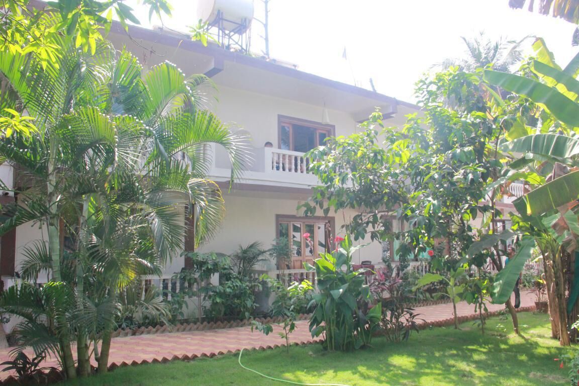 A two-story building with a balcony, surrounded by lush greenery and a well-maintained garden.