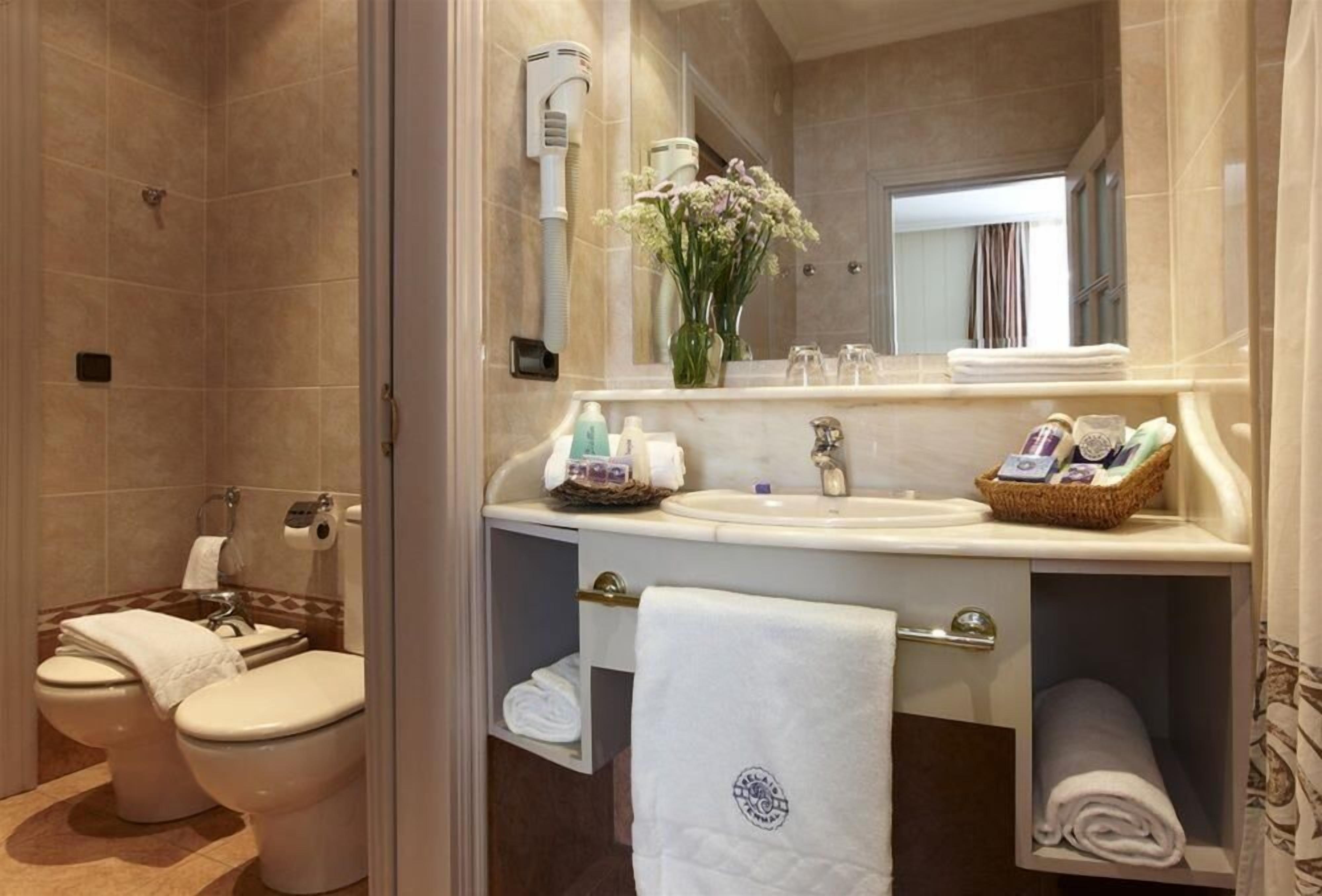 A modern bathroom with a shower, two toilets, a sink, and a vanity with towels and toiletries.