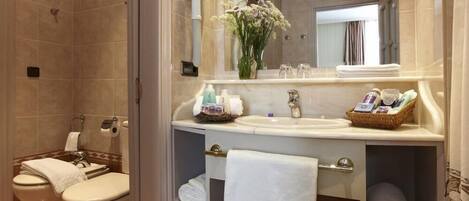 A modern bathroom with a shower, two toilets, a sink, and a vanity with towels and toiletries.