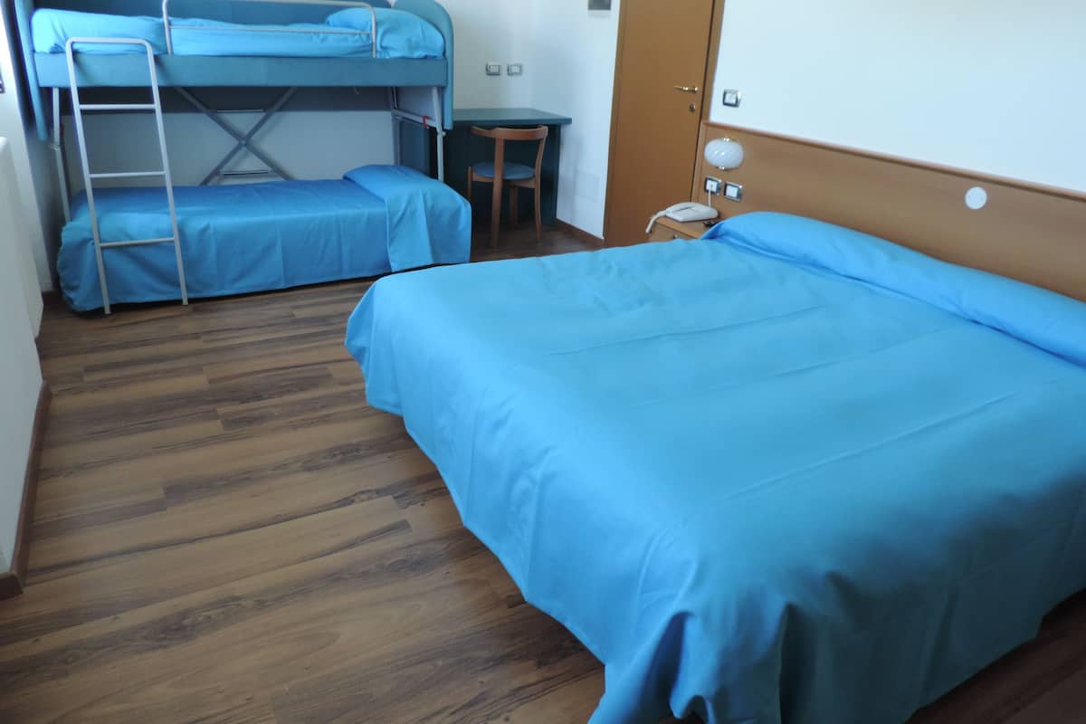 A room with two bunk beds, a small table, a chair, and a bedside table with a lamp.
