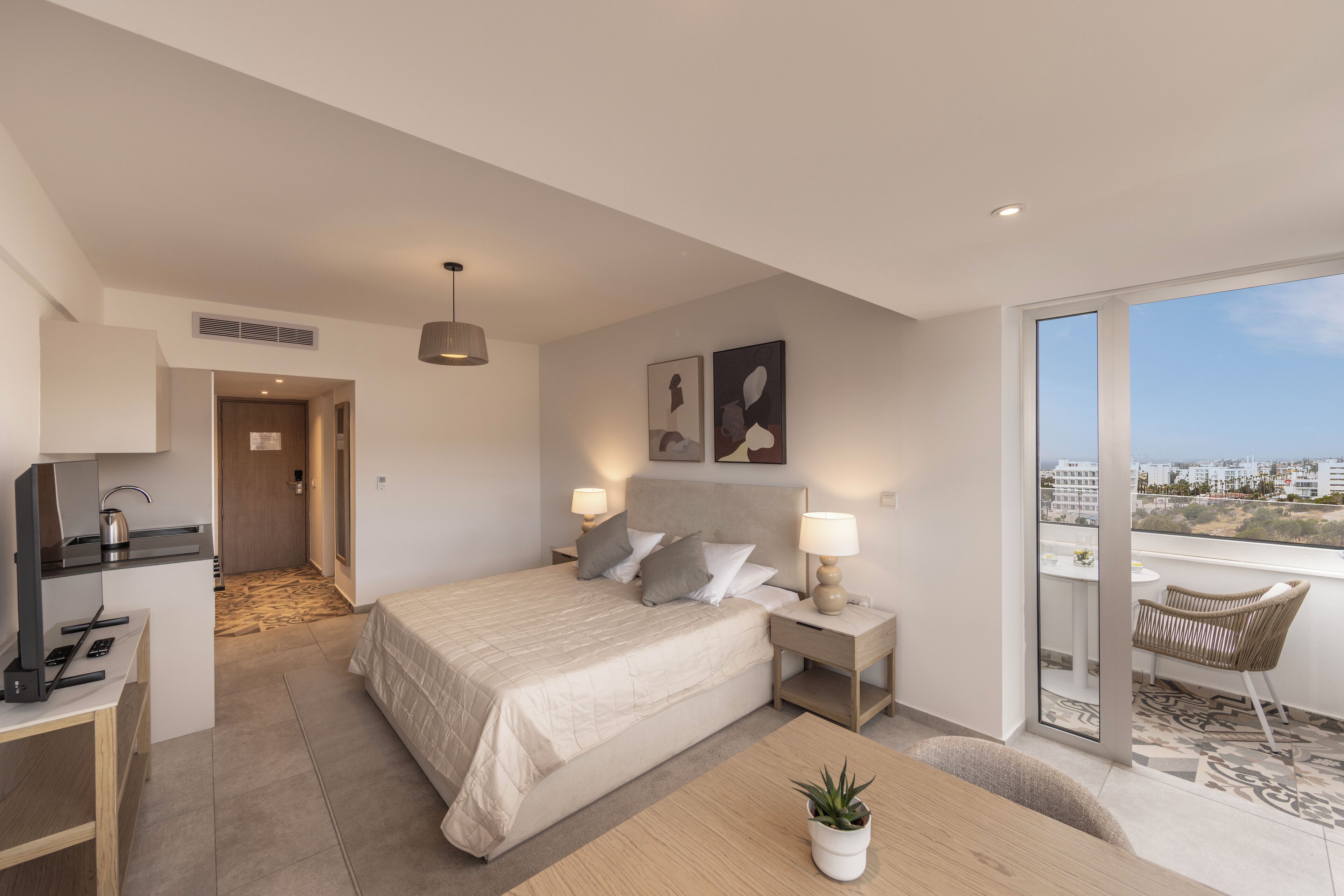Une chambre d’hôtel moderne dotée d’un grand lit, de tables de chevet avec des lampes, d’un bureau avec une bouilloire, d’une chaise et d’un balcon avec vue.