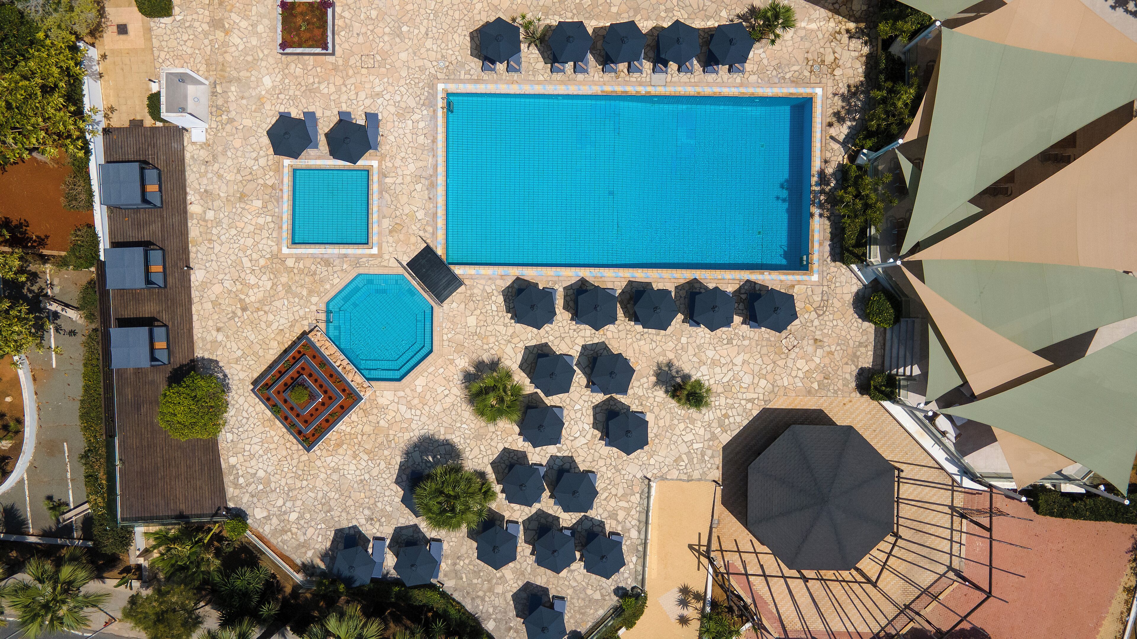 An aerial view of a resort with a large swimming pool, multiple sun loungers, and a small children's pool.