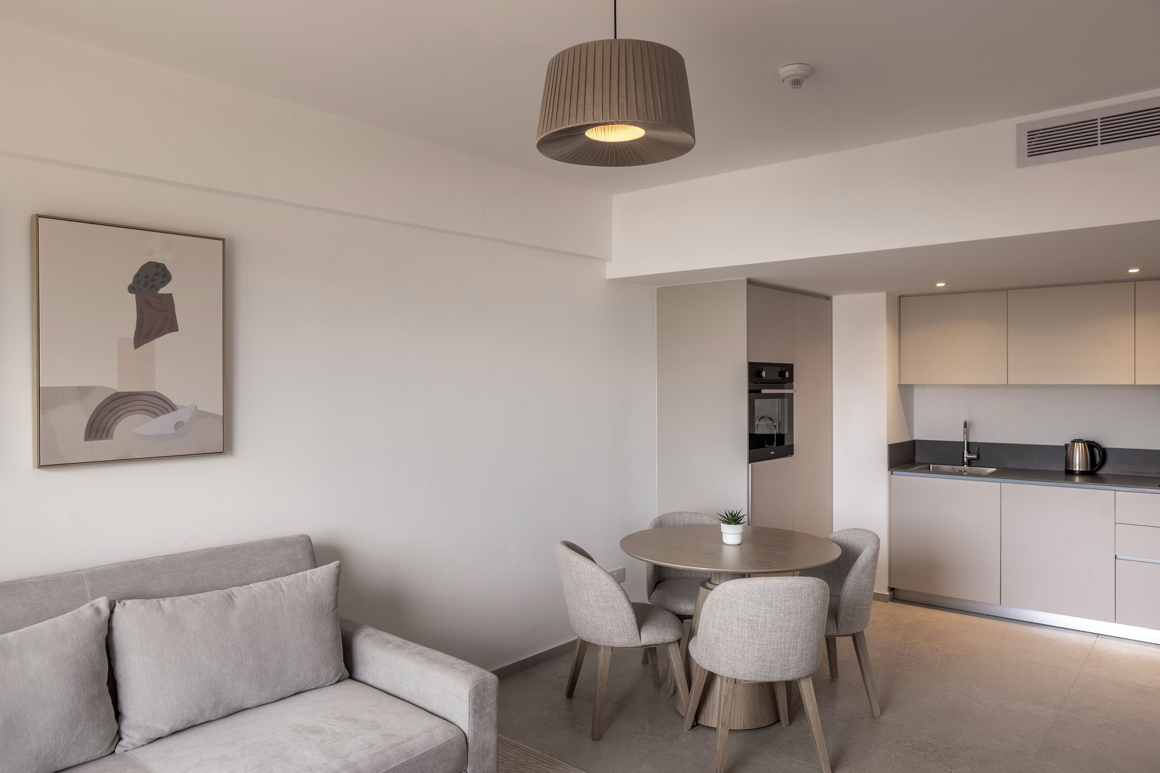 Un salon moderne comprenant un canapé, une table à manger avec des chaises, un luminaire suspendu et un coin cuisine avec des placards et des appareils électroménagers.