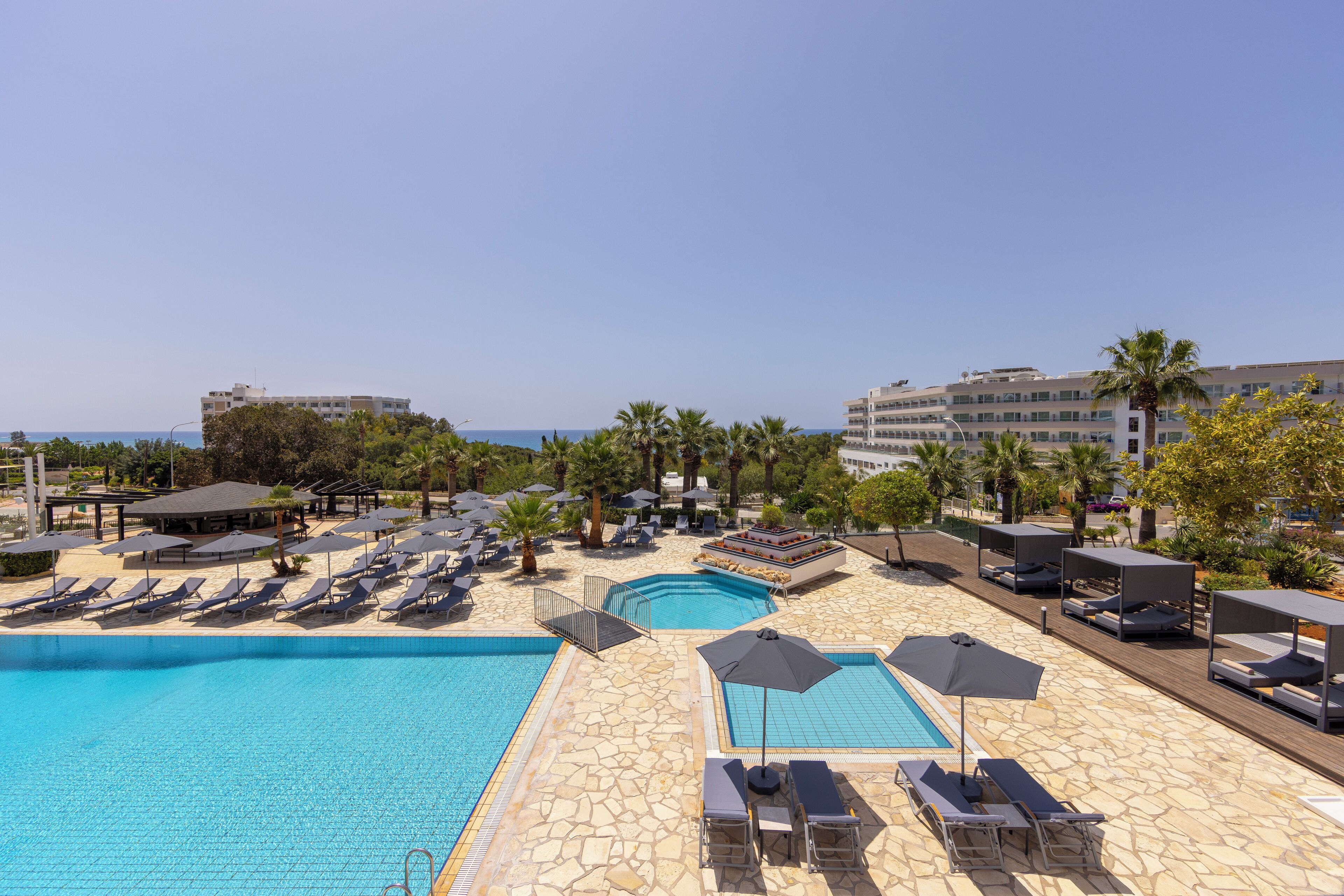 Zona de piscina en un resort con múltiples sillones de descanso y sombrillas, una piscina pequeña y vistas al mar.