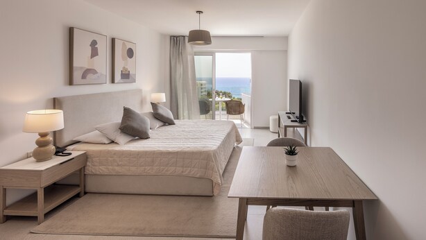 A modern hotel room with a bed, bedside table, lamp, TV, and a view of the ocean. - Cyprotel Florida Hotel (Ayia Napa)