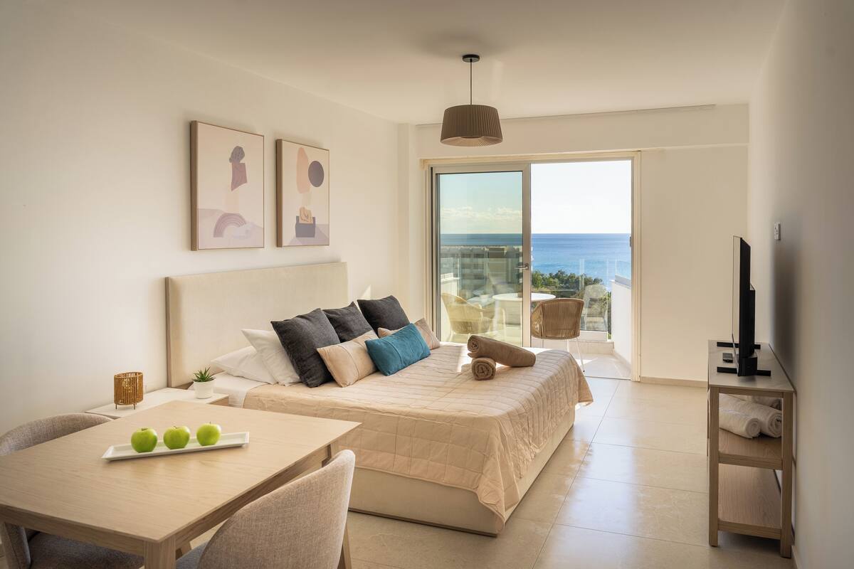 A modern bedroom with a large bed, a dining table, and a TV.