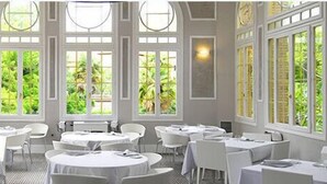 A bright, sunlit room with large windows, white tables, and chairs arranged for dining. - Hotel Parque - Balneario Termas Pallares (Alhama de Aragon)