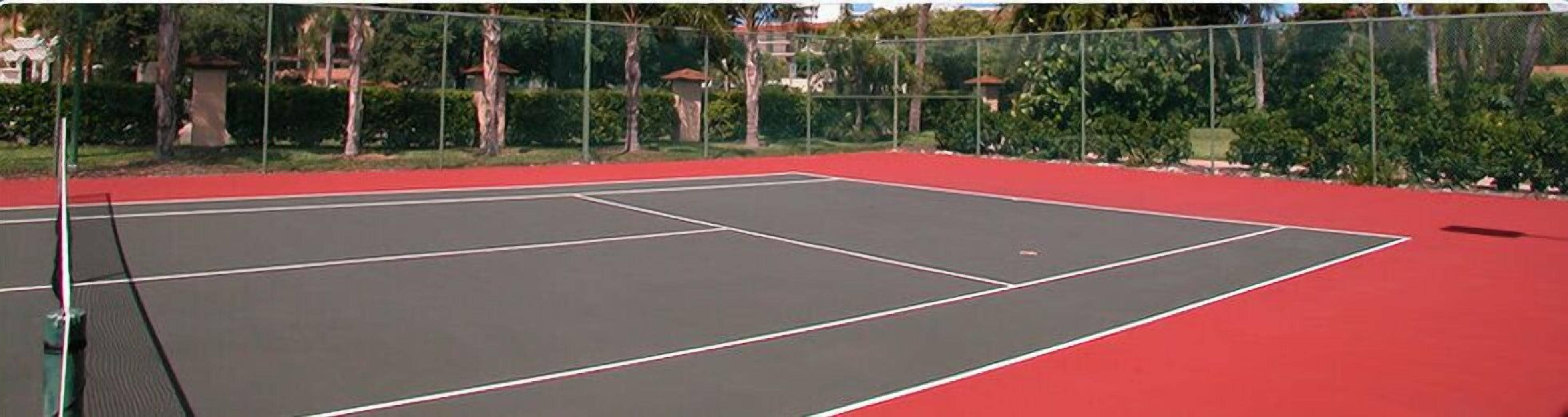 An outdoor tennis court with a red surface and a net.