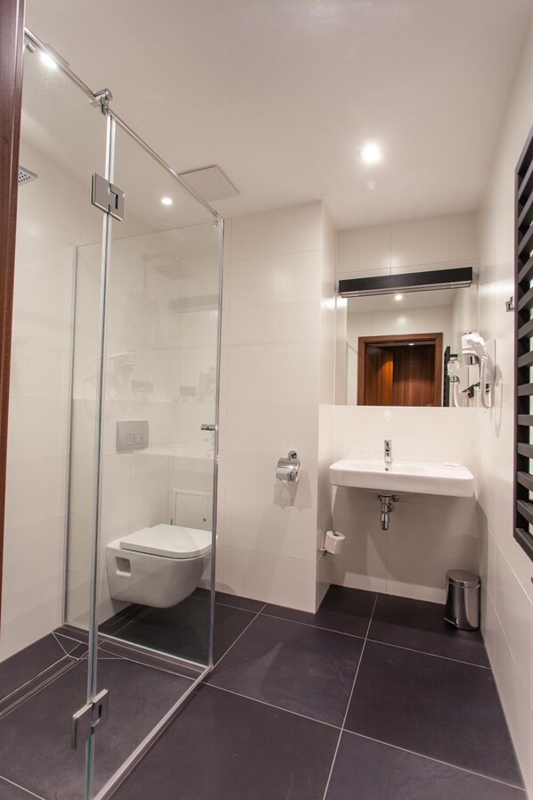 Une salle de bain moderne avec une douche à parois de verre, des toilettes blanches, un lavabo avec un miroir au-dessus et une poubelle.