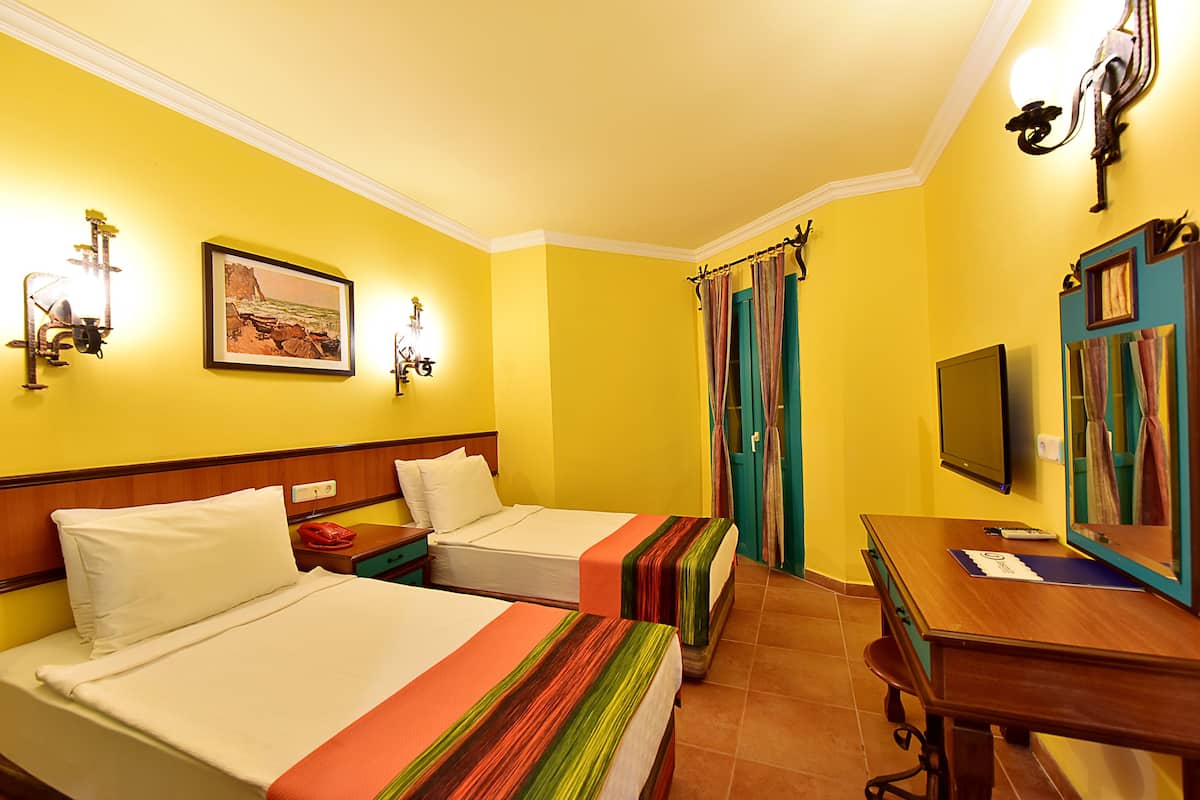 A hotel room with two beds, a desk, a television, and a painting on the wall.
