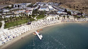 An aerial view of a coastal resort with a beach, a marina, and a hilly backdrop.