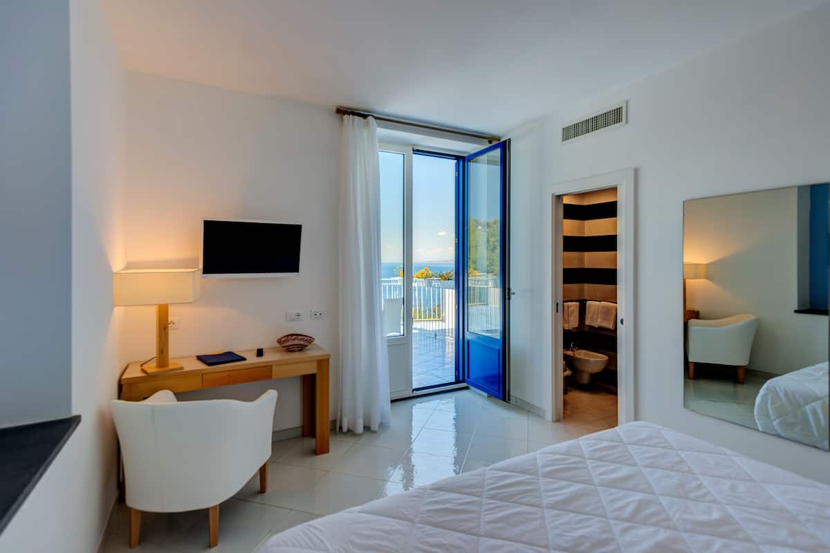 Habitación de hotel con cama, escritorio con lámpara, silla, televisor y baño visible a través de una puerta abierta.