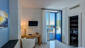 Une chambre d’hôtel équipée d’un bureau, d’une chaise, d’une télévision et d’un balcon avec vue sur la mer.
