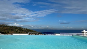 Un ciel bleu azur parsemé de nuages, une piscine et une vue sur l’océan et la terre au loin.