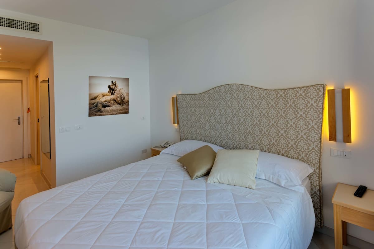 Una cama bien hecha con un cabecero estampado, una mesita de noche con un control remoto y un cuadro en la pared.