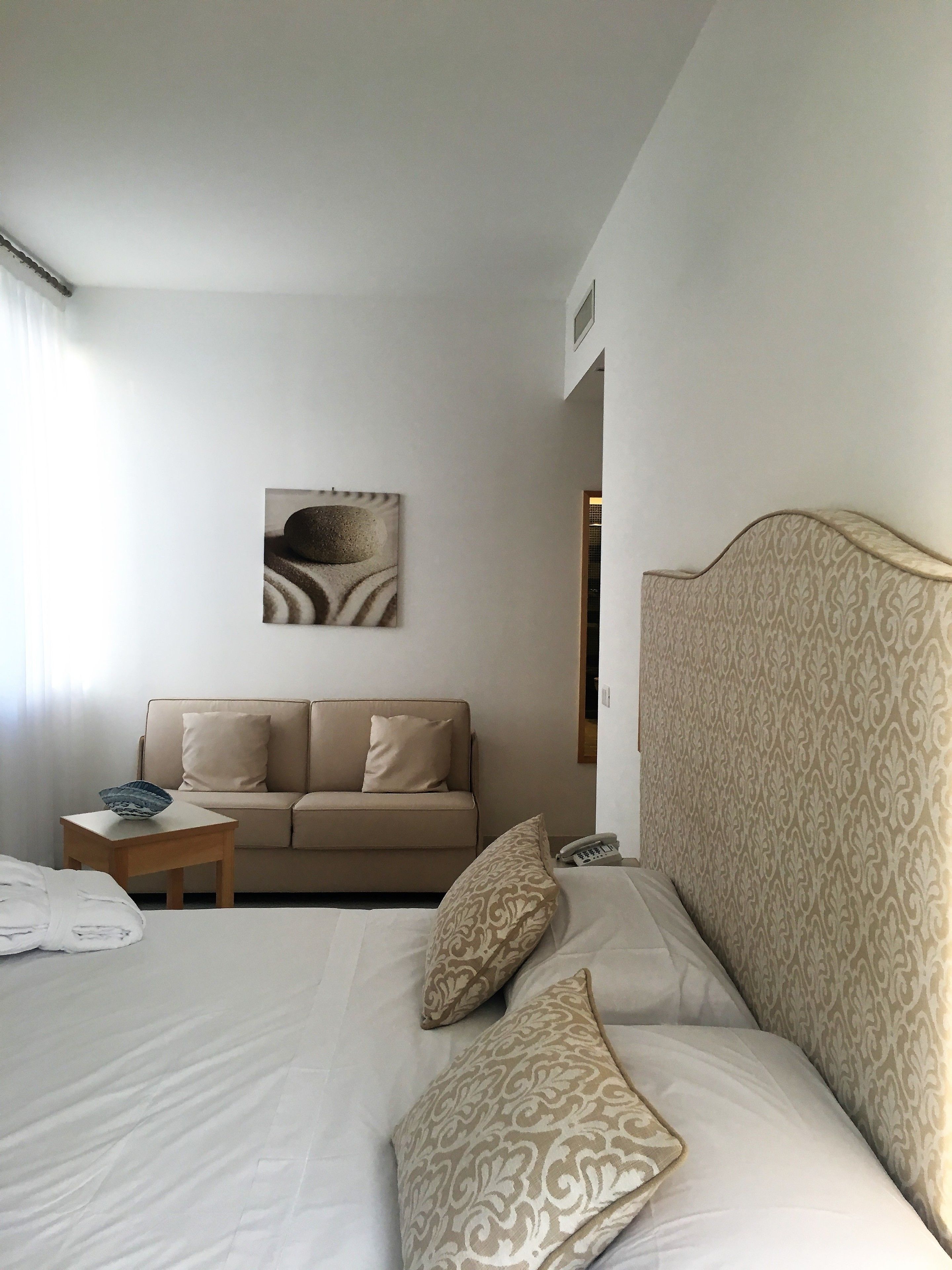 A hotel room with a bed, a sofa, a small table, and a wall-mounted artwork.