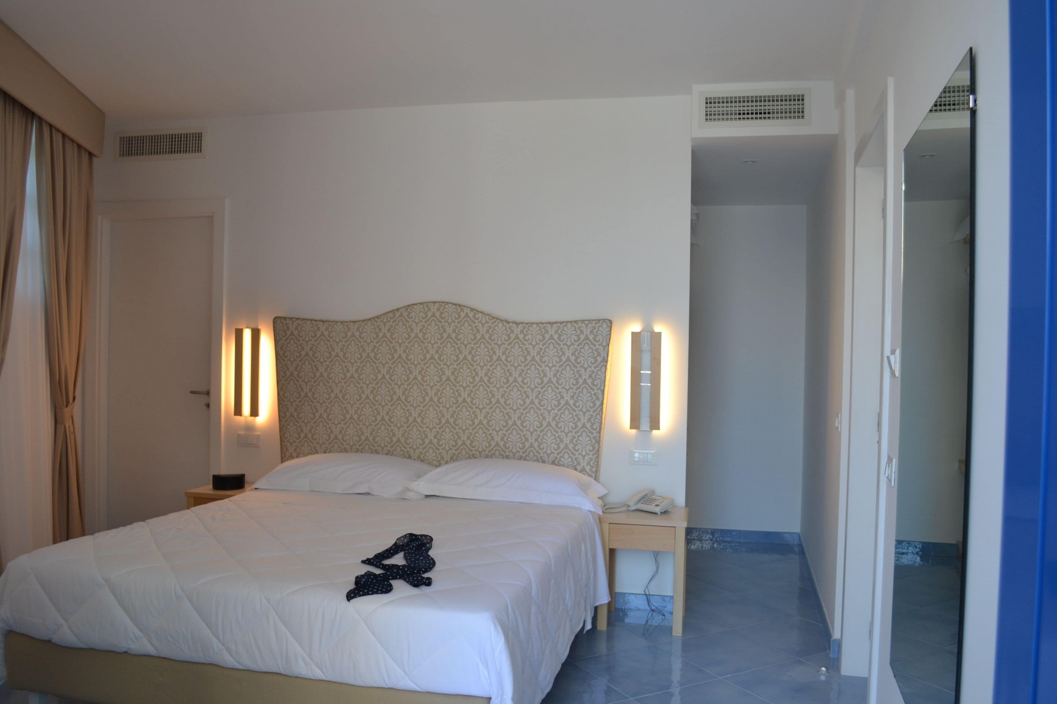 A hotel room with a bed, bedside lamps, a telephone, and a door leading to another room.