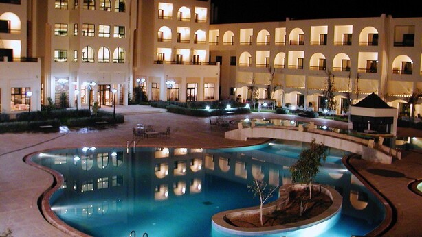A large indoor swimming pool with a fountain, surrounded by a courtyard with multiple buildings. - Hotel Gafsa Palace (Ksar)