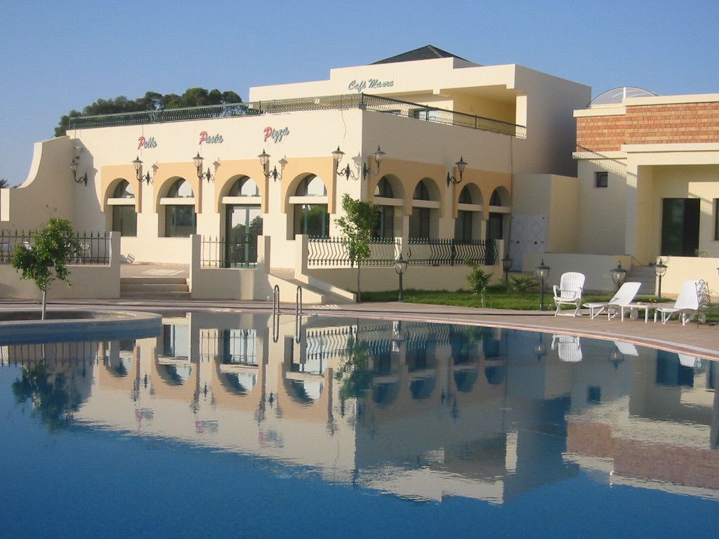 A hotel with a pool, outdoor seating, and a clear sky.