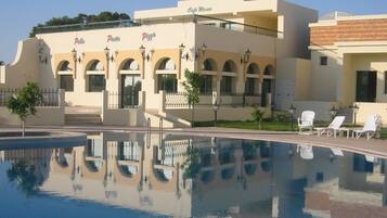 A hotel with a pool, outdoor seating, and a clear sky.