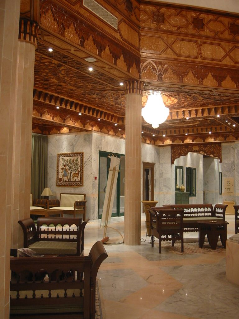 An interior with ornate wooden ceiling, marble walls, and furniture.