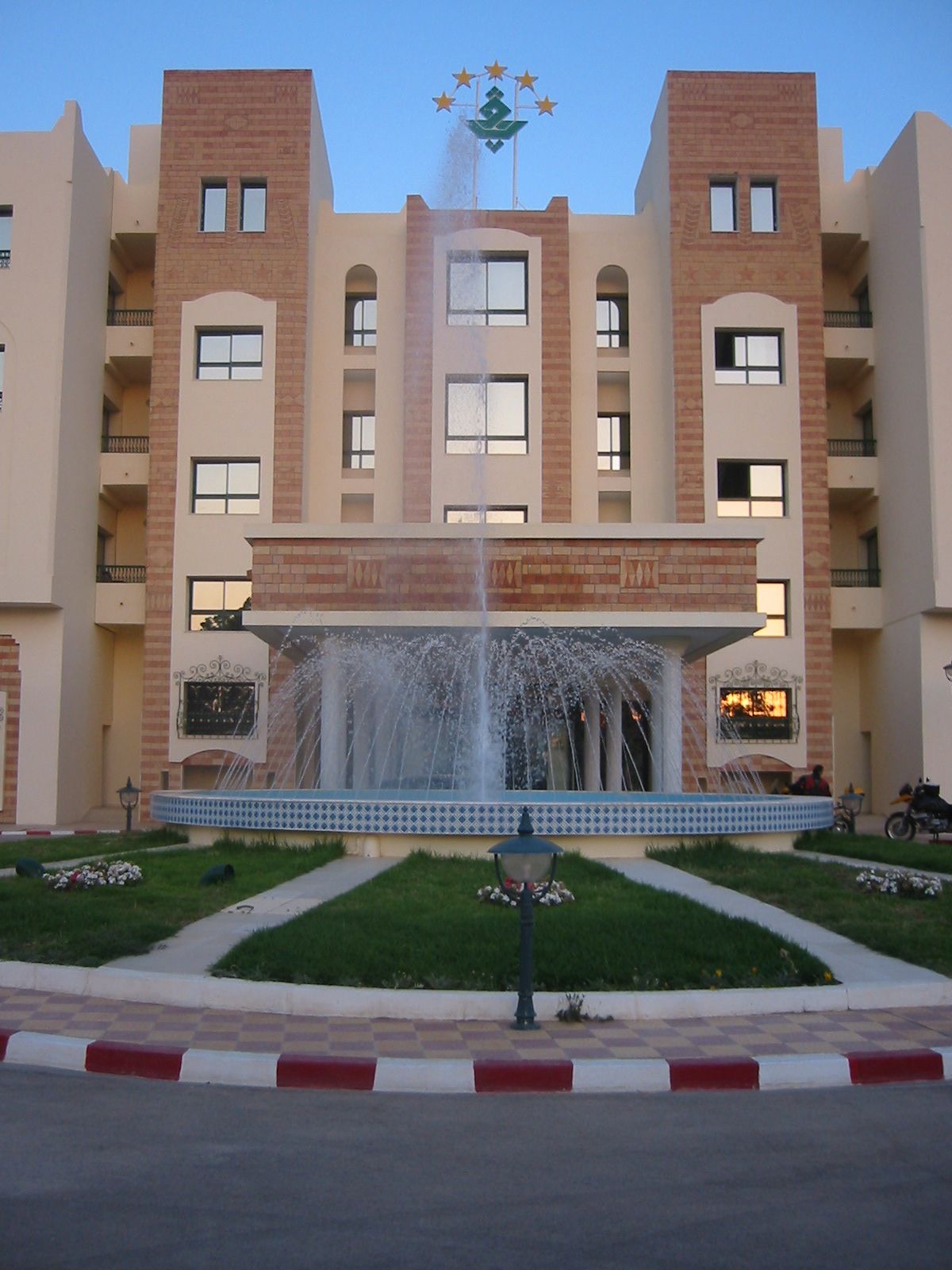 A multi-story building with a central fountain, balconies, and a clear sky.