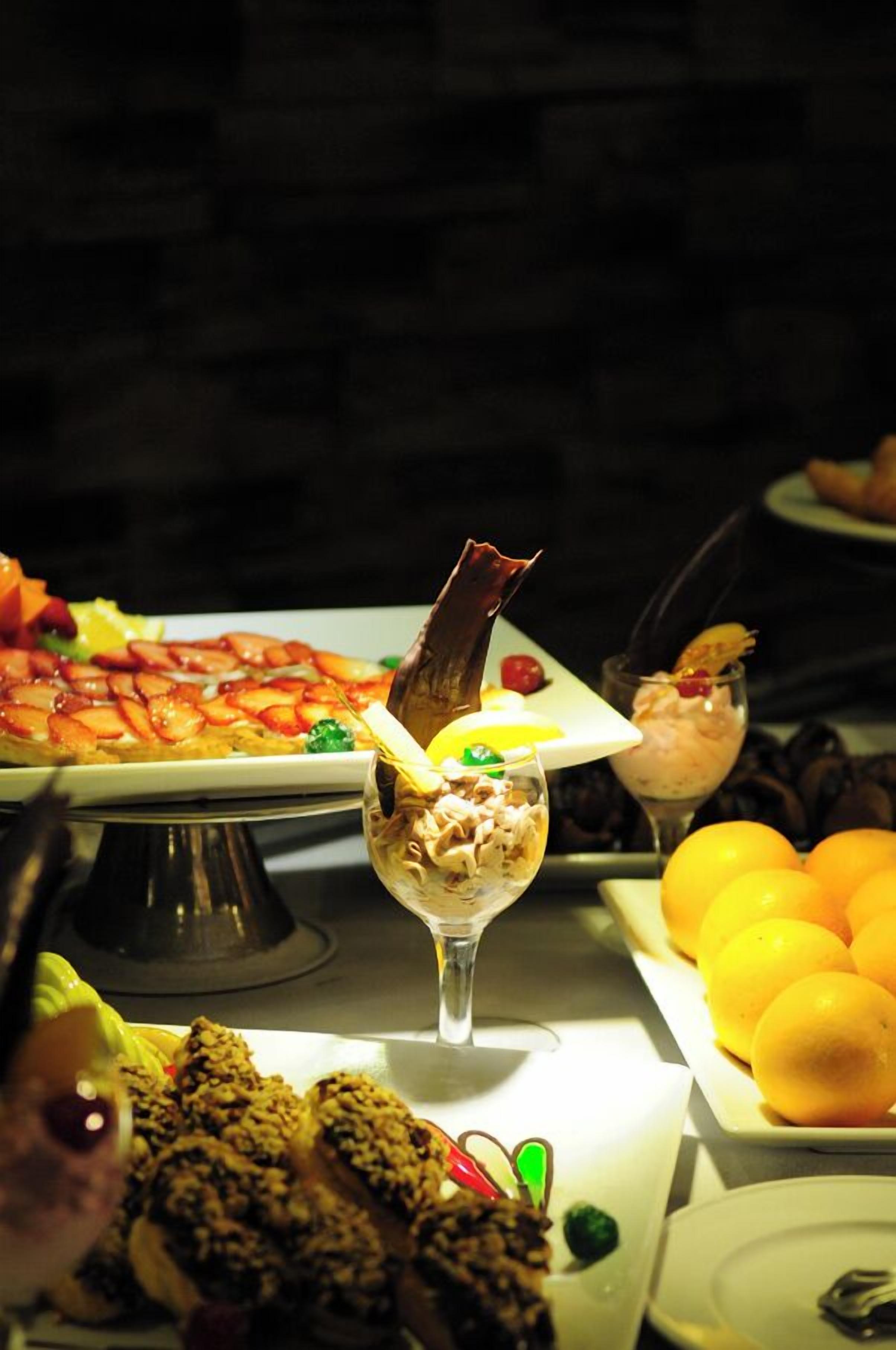 Una mesa de buffet con diversos platos, incluyendo un pastel con fruta, un postre de chocolate y un plato de naranjas.