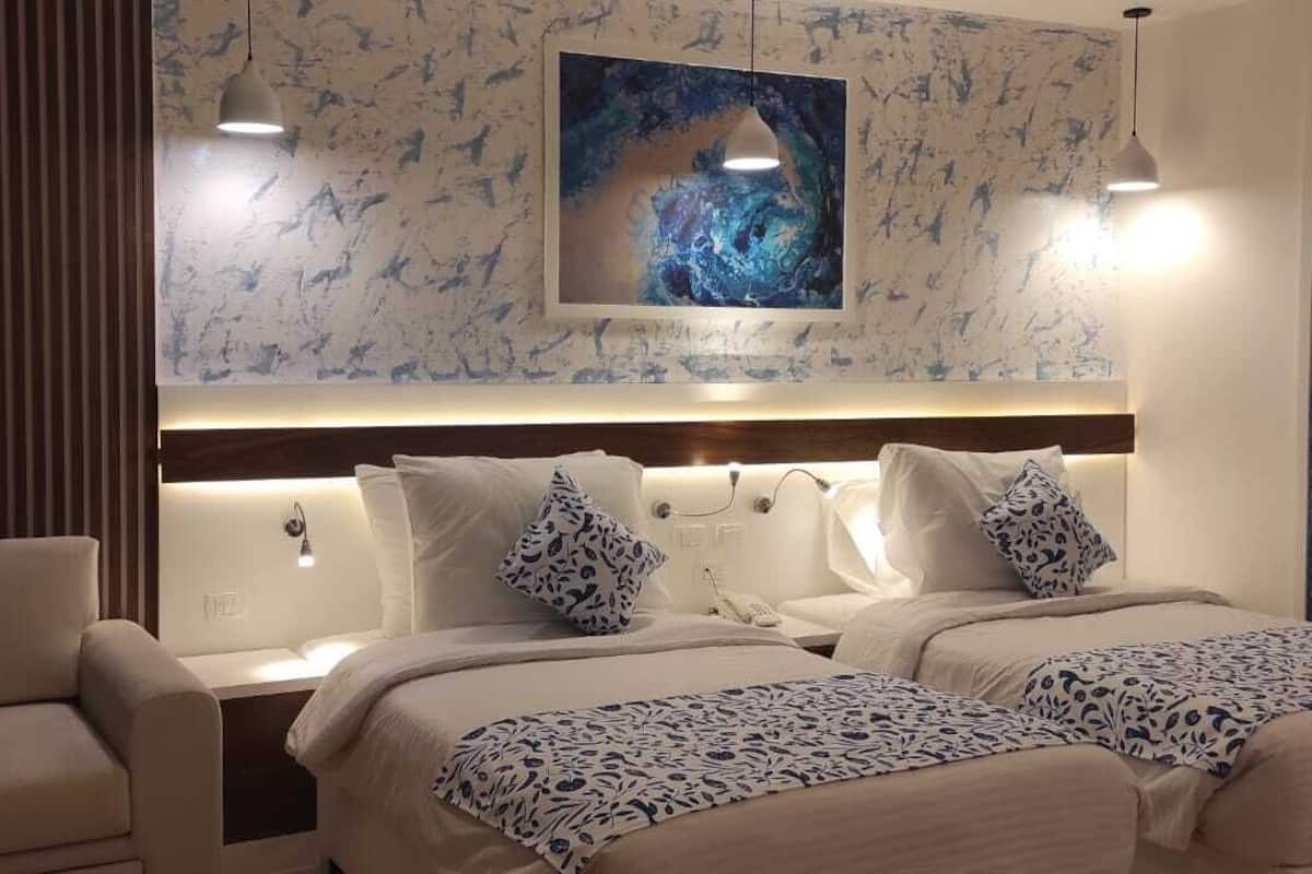 Une chambre d’hôtel avec deux lits, un canapé et un grand tableau abstrait accroché au mur.