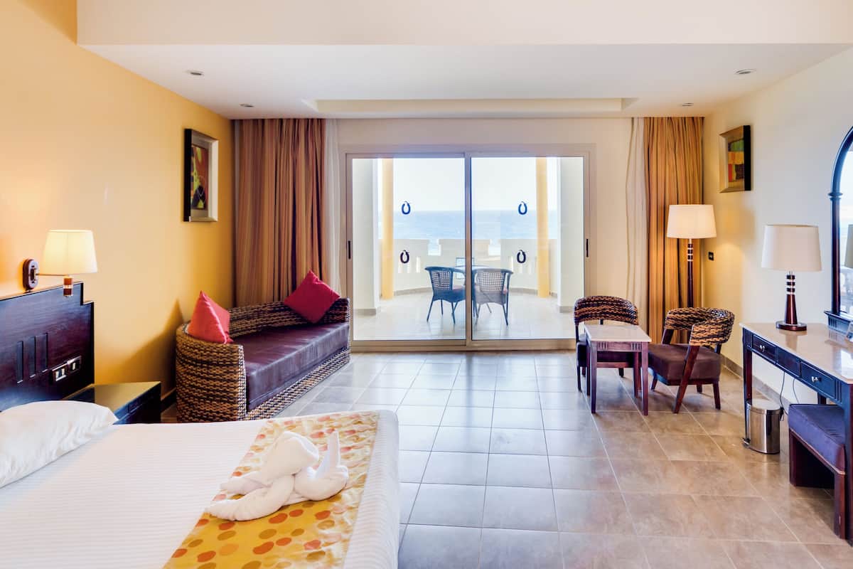 Une chambre d’hôtel comprenant un lit, un bureau, une chaise, un canapé, un balcon avec une table et des chaises, et une vue sur la mer.