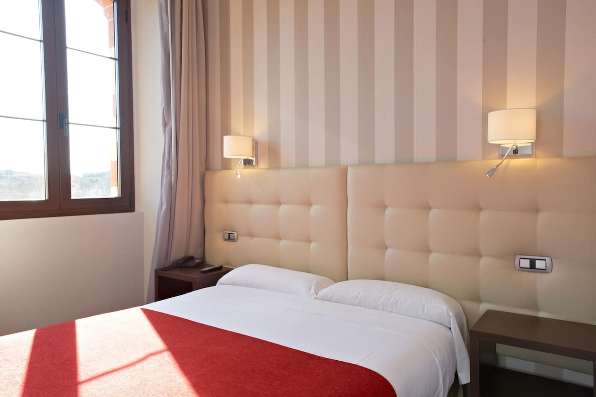 A hotel room with a large bed, two bedside tables, a window with curtains, and two wall-mounted lamps.