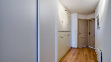 Un pasillo estrecho con suelo de madera, paredes blancas y una puerta al final.