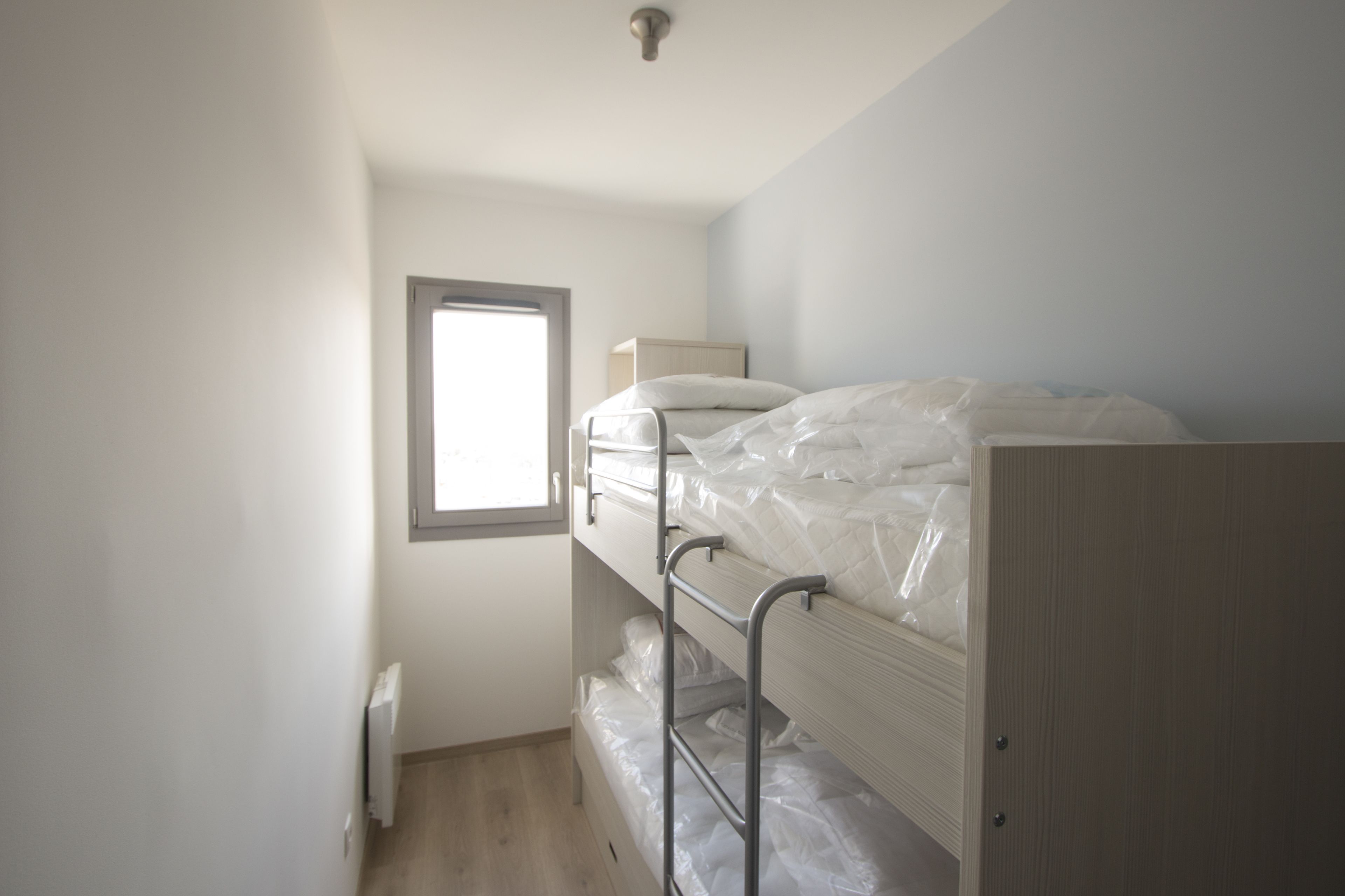 Een slaapkamer met een stapelbed, een raam, een radiator en een houten garderobe.