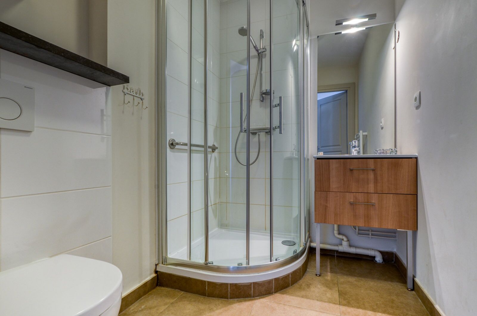 Ein modernes Badezimmer mit einer Duschkabine aus Glas, einer weißen Toilette und einem Holzkosmetikschrank mit Spiegel.