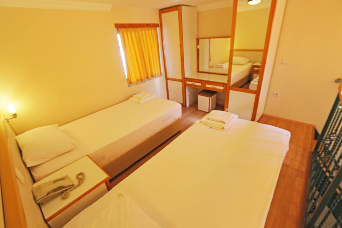 A hotel room with two single beds, a small desk with a telephone, and a mirror above the desk.