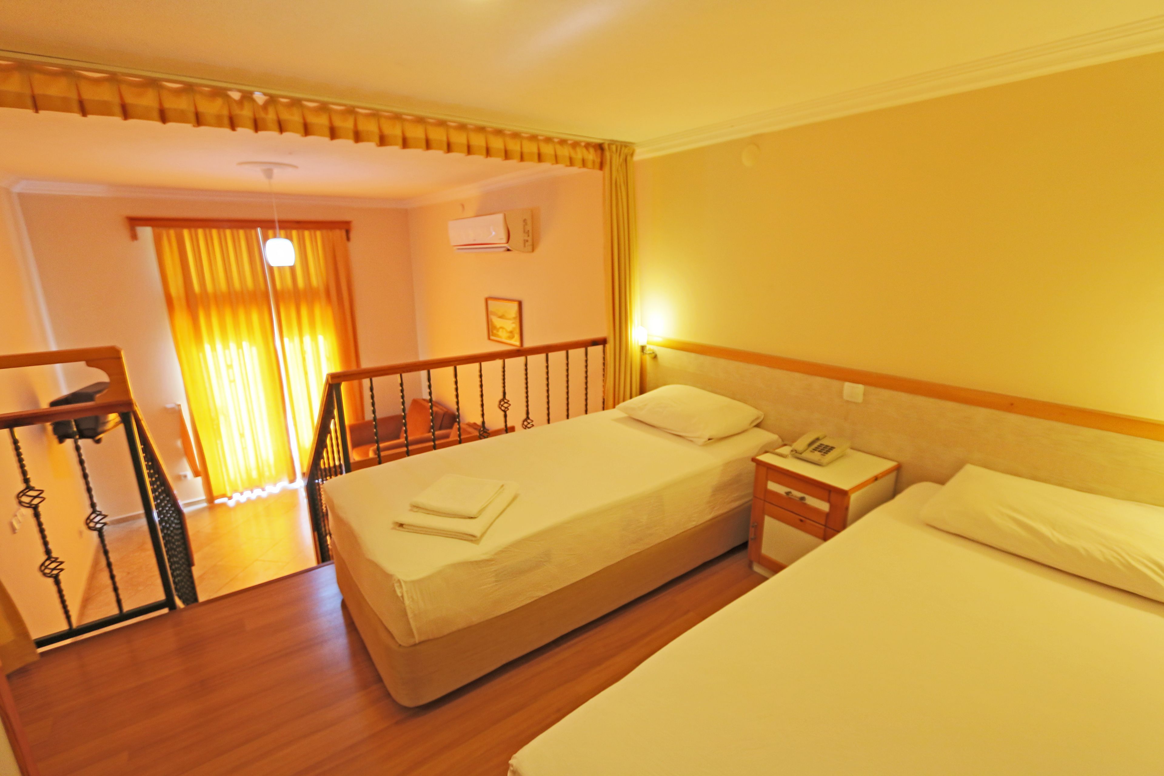 A hotel room with two beds, a wooden floor, a staircase, and a view of the hallway.