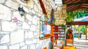 A covered outdoor seating area with stone walls, wooden furniture, and a bookshelf. - Green House Apart Hotel (Bodrum)
