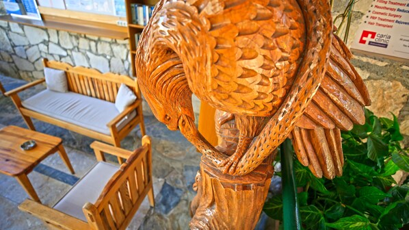 A wooden sculpture of a fish with intricate carvings, a stone wall, and wooden furniture in the background.