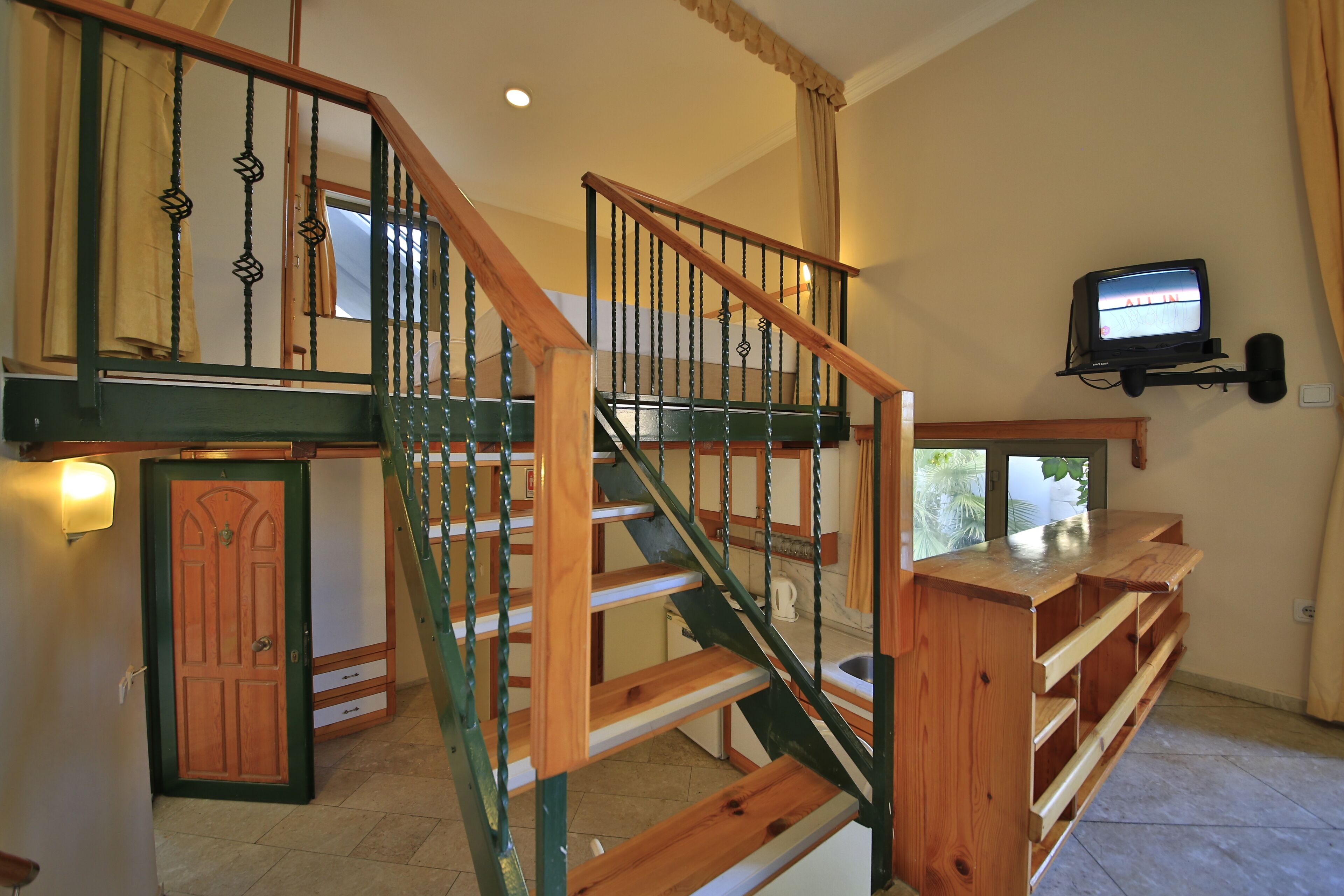 A wooden staircase with a green railing, a television mounted on the wall, and a wooden door.