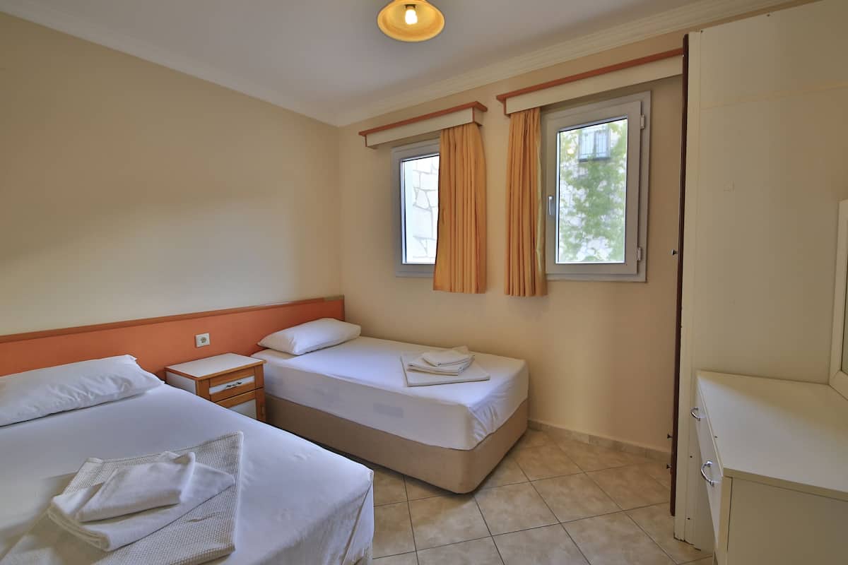 A hotel room with two beds, a small bedside table, a TV, and a window with curtains.